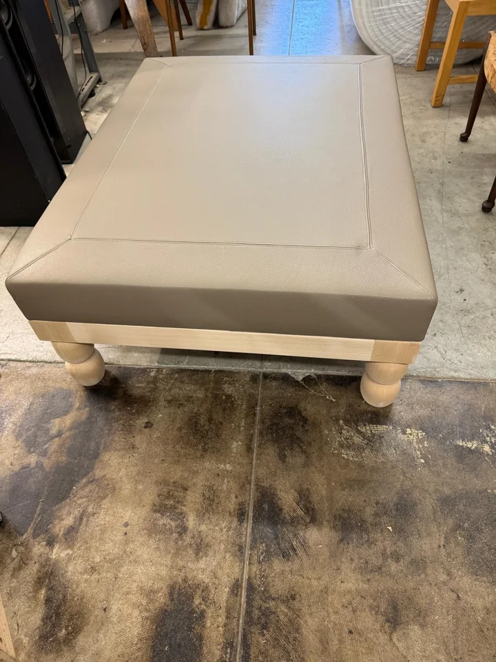 Rectangular taupe upholstered ottoman with inset stitching and pale wooden legs