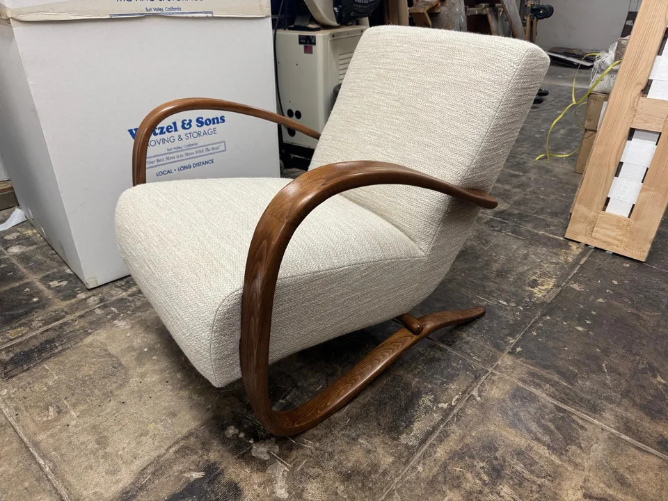 Cream upholstered lounge chair with curved wooden arms and a sculpted base