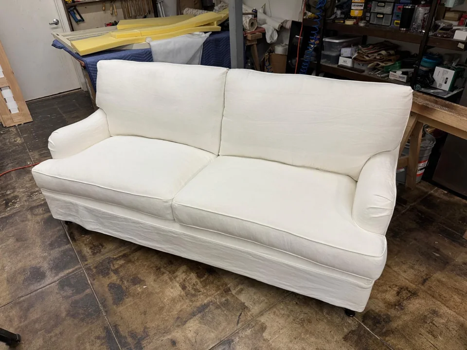 Cream two-seat sofa with upholstered arms and a skirted base in the workshop