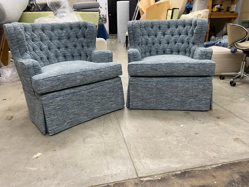 Two finished blue upholstered armchairs with button-tufted backs and skirted bases